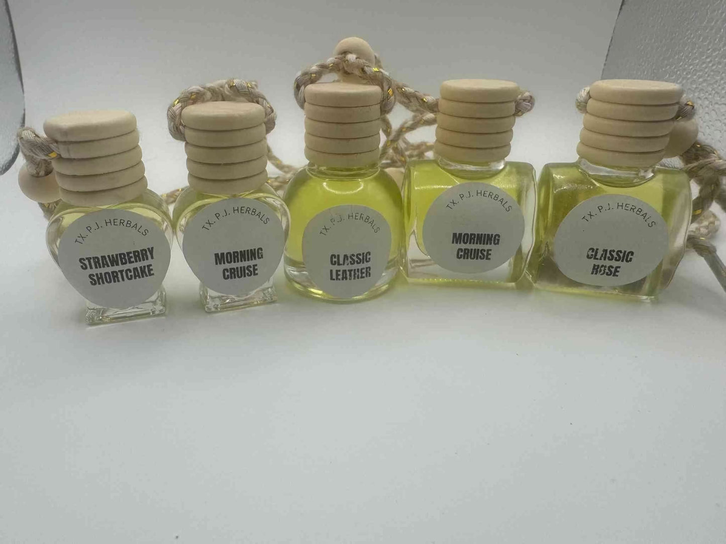 All natural car air fresheners in glass bottles with wooden lids and hanging cords, available in various scents.