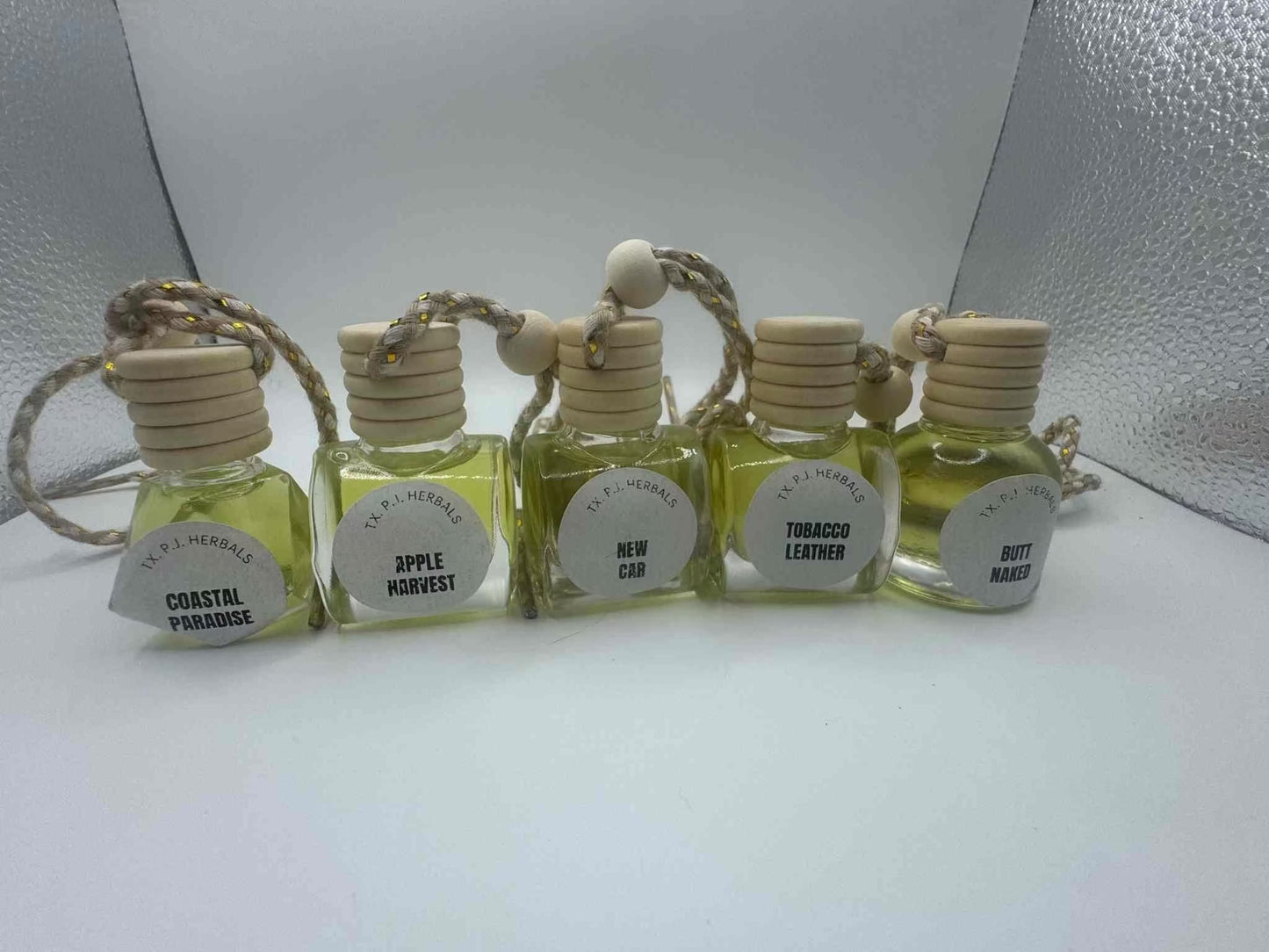 Set of all natural car air fresheners with wooden lids and essential oil scents including Coastal Paradise, Apple Harvest, New Car, Tobacco Leather, and Butt Naked.
