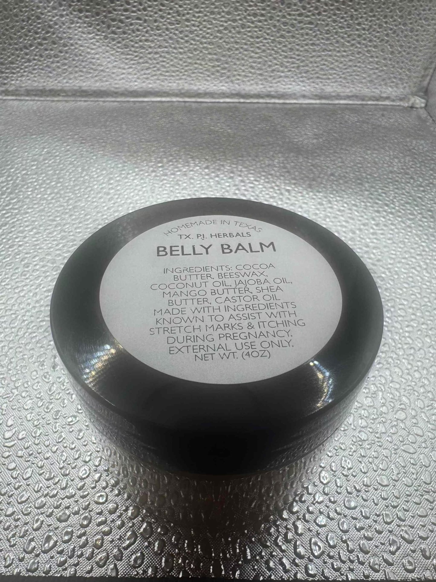 Black jar of All-Natural Belly Balm for reducing stretch marks and soothing itching during pregnancy on textured surface